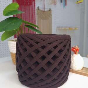 May include: A dark brown cylindrical basket constructed from thick, woven fabric strips arranged in a repeating diagonal lattice pattern. The basket features an open-top design with a consistent, uniform structure throughout its exterior surface.