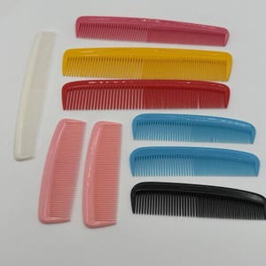 May include: A collection of colorful hair combs in various shades, including pink, yellow, red, blue, and black. The combs are arranged on a white surface, showcasing their different shapes and sizes. The image highlights the variety of colors and styles.