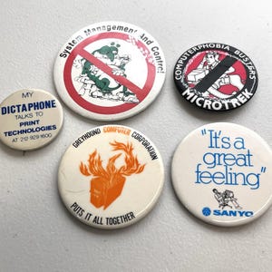 May include: A collection of vintage round pinback buttons with various designs and text. One button reads "MY DICTAPHONE" and another says "System Management And Control!". Other buttons include "COMPUTERPHOBIA BUSTERS" and "It's a great feeling".
