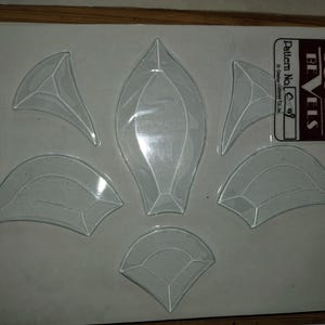May include: A sheet of clear glass bevels in geometric shapes, including teardrops, triangles, and curved segments. The sheet has a sticker that reads "SUPER BEVELS" and "Pattern No. C-09".