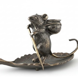 Könnte beinhalten: Bronze-Mausfigur mit Rucksack und Wanderstab, die auf einer blattförmigen Schale steht. Die Maus hat detailliertes Fell und ist so positioniert, als würde sie reisen. Die Blattschale hat komplizierte Aderdetails.
