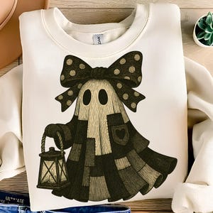 May include: White sweatshirt featuring a whimsical ghost design. The ghost has a large polka-dot bow, a patchwork-style body, and is holding a lantern. The design incorporates black, tan, and cream colors, perfect for Halloween.
