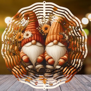 Op de afbeelding: Decoratieve houten uitsparing met twee kabouters met witte baarden, gekleed in oranje en rode hoeden en outfits. De kabouters zijn omgeven door herfstbladeren en bloemen, met een geschulpte rand.