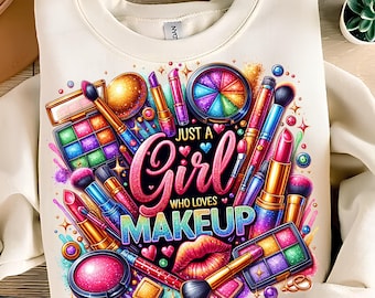 May include: Cream-colored sweatshirt featuring a colorful makeup design. The graphic includes makeup brushes, lipsticks, eyeshadow palettes, and the text "Just a Girl Who Loves Makeup" in a vibrant, glittery font. The design is surrounded by hearts and stars.