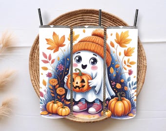 May include: White tumbler with a cartoon ghost in an orange beanie, holding a jack-o'-lantern. The design includes autumn leaves, flowers, and pumpkins. The tumbler has a black straw and is set in a woven basket.
