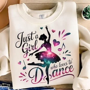 May include: Cream-colored sweatshirt featuring a ballerina silhouette with a galaxy-themed tutu. The text "Just a Girl who loves to Dance" is displayed in a cursive font, along with musical notes and heart shapes.