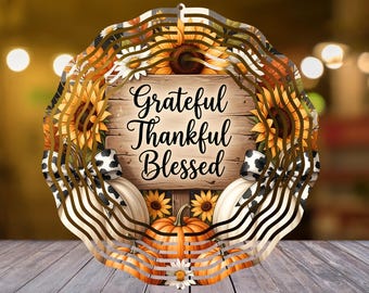Peut inclure: Un carillon à vent circulaire en métal avec une plaque centrale en bois portant le texte Grateful Thankful Blessed. Le motif comprend des tournesols jaunes, des marguerites blanches, des citrouilles orange et blanches avec des nœuds à motifs vache.