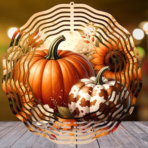 Op de afbeelding: Een ronde metalen windspinner met een bedrukt ontwerp van een grote oranje pompoen en een kleinere witte pompoen met bruine koeienvlekken, omringd door gele zonnebloemen, witte bloemen en herfstbladeren met een geschulpte rand.