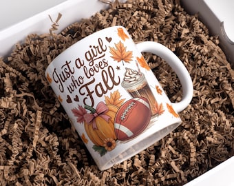 May include: White ceramic mug with the text "Just a girl who loves Fall", a pumpkin, football, and a coffee drink. The mug is inside a white box filled with brown packing material.
