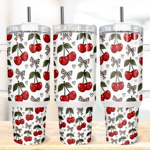 Puede incluir: Tres tazas de viaje blancas con un estampado de cerezas. El diseño presenta cerezas rojas, hojas verdes, lazos con estampado de leopardo en blanco y negro y pequeños corazones negros. Cada taza tiene una tapa transparente, una pajita plateada y un asa blanca.