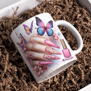 Könnte beinhalten: Weiße Keramik-Tasse mit einer Hand mit langen, rosa, floral verzierten Nägeln, Schmetterlingen und einer Flasche rosa Nagellack. Die Tasse befindet sich in einer weißen Schachtel mit braunem Papier. Die Tasse hat einen weißen Griff.