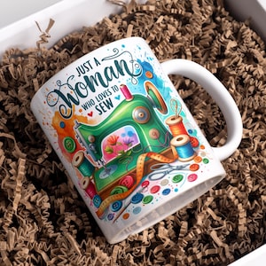 Könnte beinhalten: Weiße Keramik-Tasse mit einer farbenfrohen Illustration einer Nähmaschine, Garnrollen und Knöpfen. Auf der Tasse steht der Text "Just a Woman Who Loves to Sew". Die Tasse befindet sich in einer weißen Box mit braunem Verpackungsmaterial.