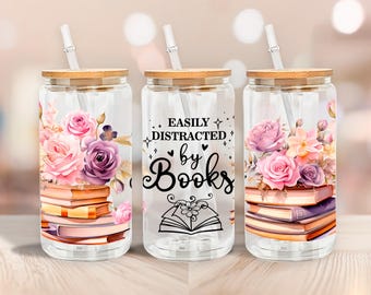Könnte beinhalten: Drei transparente Glasbecher mit Bambusdeckeln und Strohhalmen. Jeder Becher hat ein Blumendesign mit rosa und lila Rosen und einem Stapel Bücher. Der mittlere Becher hat den Text "EASILY DISTRACTED by Books".