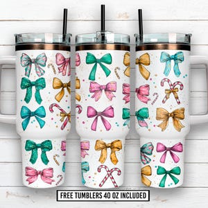 Puede incluir: Tres vasos blancos de 1,18 litros con borde color cobre, pajita negra y asa. Cada vaso presenta un patrón repetido de lazos coloridos y bastones de caramelo. El texto "FREE TUMBLERS 40 OZ INCLUDED" está en la parte inferior.