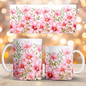 Puede incluir: Tazas de café de cerámica blanca con un diseño floral de margaritas rosas. Las margaritas tienen centros amarillos y están rodeadas de hojas verdes y pequeñas flores blancas. También se muestra un diseño rectangular a juego.