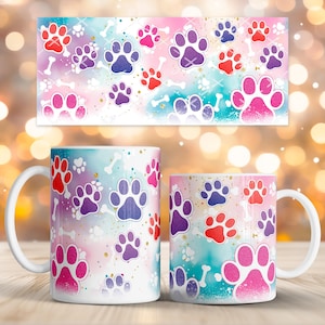 Puede incluir: Dos tazas de cerámica blanca con un diseño colorido de huellas de patas. El diseño presenta huellas de patas rosas, moradas y rojas y formas de huesos blancos sobre un fondo de acuarela. Un diseño rectangular a juego está encima de las tazas.