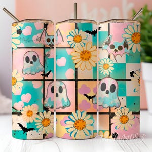Puede incluir: Un vaso cilíndrico con pajita de metal que presenta un patrón de cuadrícula de cuadrados en rosa pastel, turquesa y amarillo. El diseño incluye ilustraciones de fantasmas blancos, margaritas amarillas, corazones rosas y murciélagos negros.