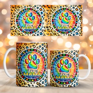 Puede incluir: Dos tazas de café con asa blanca con un diseño de huella de pata colorida. El diseño presenta un efecto tie-dye con colores arcoíris y las palabras "Dog Mama". Las tazas tienen un fondo con estampado de leopardo.