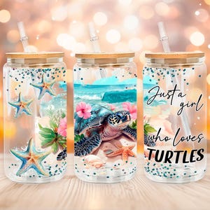 Puede incluir: Tres vasos de vidrio transparente con tapas y pajitas de bambú. Los vasos presentan diseños con temática marina, incluyendo estrellas de mar, una tortuga marina y el texto "Just a girl who loves TURTLES". Los diseños son en tonos azules, rosas y verdes.
