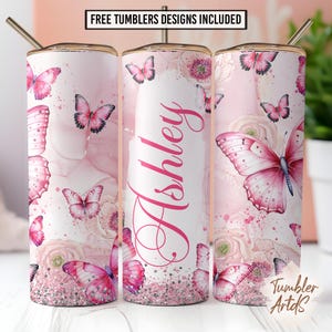 May include: A personalized tumbler featuring a pink butterfly design. The tumbler has a white background with the name "Ashley" in pink script. Pink butterflies and floral accents decorate the tumbler. The text "FREE TUMBLERS DESIGNS INCLUDED" is at the top.