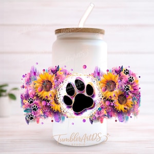 Puede incluir: Un vaso de vidrio esmerilado con tapa de bambú y pajita de vidrio transparente. El exterior presenta un diseño vibrante con girasoles amarillos, acentos florales morados y rosas, y pequeñas huellas de patas negras alrededor de un icono central.