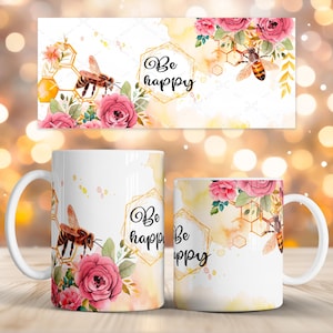 Puede incluir: Taza de cerámica blanca con una abeja, rosas rosas y un diseño de panal. La taza tiene las palabras "Be happy" en un marco geométrico dorado. El diseño se repite en un artículo rectangular a juego.
