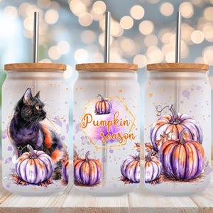 Puede incluir: Tres vasos de vidrio esmerilado con tapas de madera y pajitas de metal. Cada vaso presenta un diseño diferente: un gato negro, una calabaza con el texto "Pumpkin season" y un grupo de calabazas. Las calabazas son moradas y naranjas.