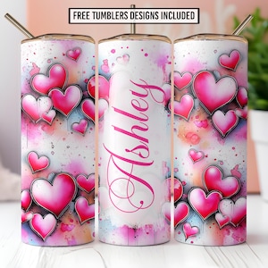 May include: A personalized tumbler featuring a design of pink hearts on a white background with watercolor splashes. The name "Ashley" is written in pink script. The tumbler includes a straw and the text "FREE TUMBLERS DESIGNS INCLUDED".