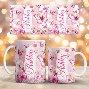 May include: Two white ceramic mugs and a matching rectangular design featuring a pink butterfly and floral pattern. The name "Ashley" is written vertically in a cursive font on the mugs and design. The design includes pink butterflies and flowers.