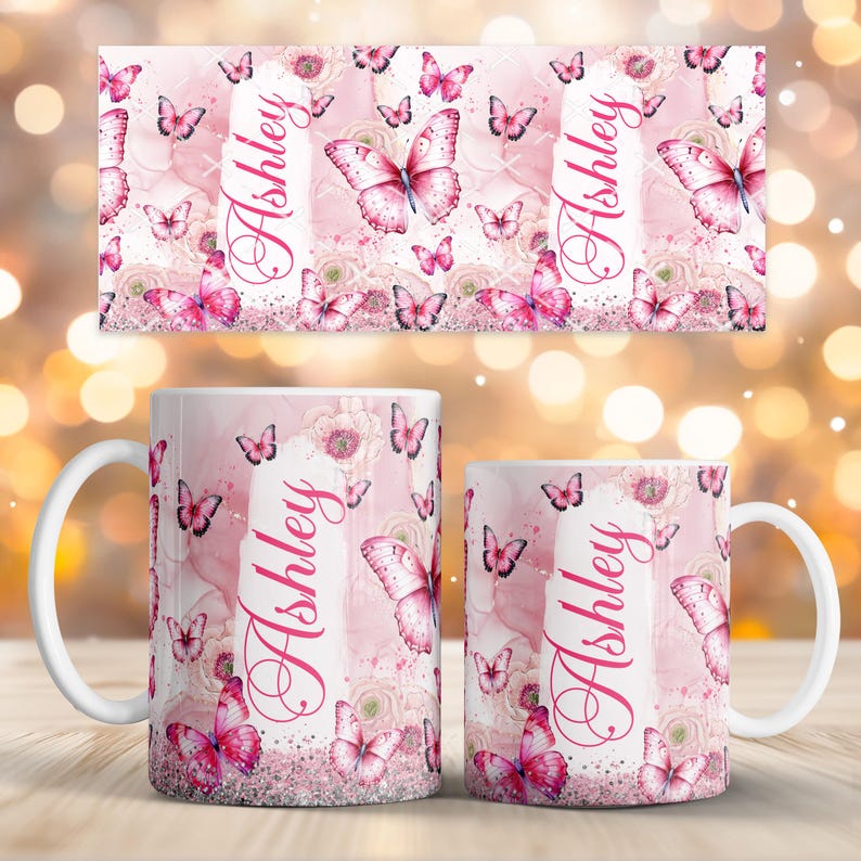 May include: Two white ceramic mugs and a matching rectangular design featuring a pink butterfly and floral pattern. The name "Ashley" is written vertically in a cursive font on the mugs and design. The design includes pink butterflies and flowers.