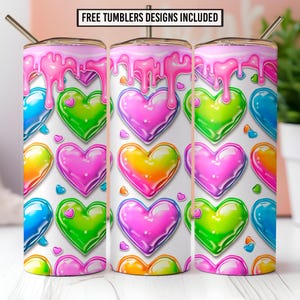 Puede incluir: Tres vasos de acero inoxidable con un diseño de glaseado rosa goteando en la parte superior. Los vasos presentan un patrón de corazones coloridos y brillantes en tonos rosa, verde, amarillo y azul. El texto "FREE TUMBLERS DESIGNS INCLUDED" está en la parte superior.