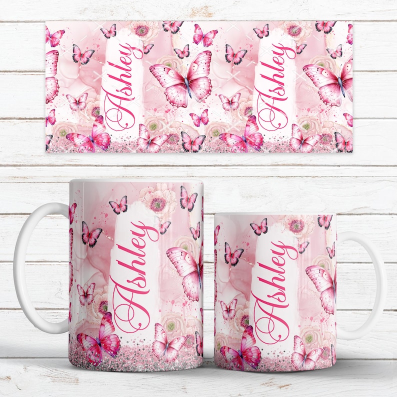 May include: Pink and white ceramic mug and matching rectangular coaster, both featuring a butterfly and floral design. The name "Ashley" is printed vertically on both items. The mug has a white handle and a glittery base.