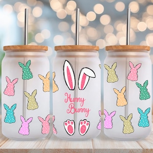 Puede incluir: Tres vasos de vidrio esmerilado con forma de lata con tapas de madera y pajitas de metal. Cada vaso presenta un tema de conejito con ilustraciones de conejitos coloridos y el texto "Hunny Bunny". Las ilustraciones de conejitos son rosas, verdes, amarillas y azules.