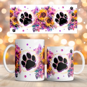 以下が含まれることがあります： 足跡のデザインが施された白いセラミックマグ。マグカップは、金色の幾何学的なフレームの中に黒い足跡があり、ヒマワリと紫の花に囲まれています。追加の足跡と紫色のドットがマグカップの周りに散らばっています。