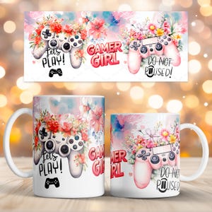 Puede incluir: Tazas de cerámica blanca con diseños florales y de mandos de videojuegos. Una taza presenta un mando con el texto "Let's PLAY!" y otra con "GAMER GIRL". Una pancarta encima de las tazas tiene el texto "DO NOT POUSED!"