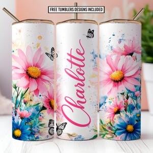 Puede incluir: Vaso blanco con un diseño floral con margaritas rosas, flores azules y mariposas. El nombre "Charlotte" está escrito en rosa. El vaso incluye una tapa y una pajita doradas. El texto en la parte superior dice "FREE TUMBLERS DESIGNS INCLUDED".