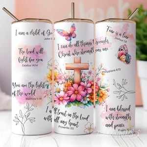 Puede incluir: Un vaso cilíndrico blanco con pajita de metal que presenta ilustraciones florales coloridas, una cruz de madera, mariposas y varias citas religiosas que incluyen I am a child of God, I can do all things through Christ y Fear is a liar.