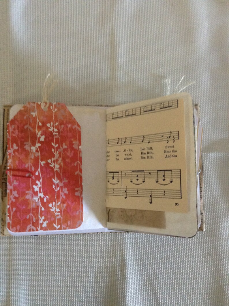 Puede incluir: Un peque&ntilde;o libro hecho a mano con una etiqueta de patr&oacute;n floral rojo y blanco unida a la portada. El libro est&aacute; abierto en una p&aacute;gina con partitura musical que presenta la letra "Sweet Allot, Ben Bolt, the wood, Ben Bolt, the school, Ben Bolt, Near the And the (3)"