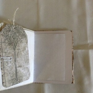 Puede incluir: Un diario abierto con una p&aacute;gina en blanco y una cubierta decorativa con un &aacute;rbol y un dise&ntilde;o vintage. La cubierta est&aacute; hecha de papel con una superficie texturizada.