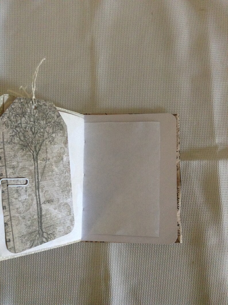 Puede incluir: Un diario abierto con una p&aacute;gina en blanco y una cubierta decorativa con un &aacute;rbol y un dise&ntilde;o vintage. La cubierta est&aacute; hecha de papel con una superficie texturizada.