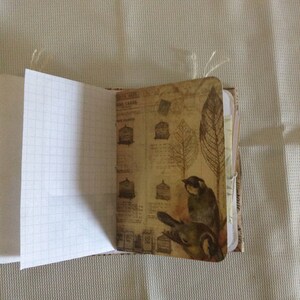 Puede incluir: Un diario de estilo vintage con una cubierta de papel marr&oacute;n con un estampado de p&aacute;jaros y hojas. El diario tiene un interior de papel cuadriculado.
