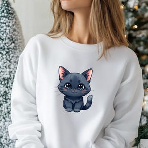 May include: White crew neck sweatshirt with a cartoon illustration of a black cat. The cat has large blue eyes and pink inner ears. The design is centered on the front of the sweatshirt.