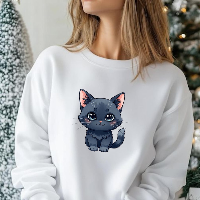 May include: White crew neck sweatshirt with a cartoon illustration of a black cat. The cat has large blue eyes and pink inner ears. The design is centered on the front of the sweatshirt.