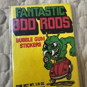 May include: A rectangular yellow package of Fantastic Odd Rods bubble gum stickers. The front features green text, red text, and a green monster illustration holding a gear shift knob while driving a red car. Text includes Gum Net Wt. 1/8 oz.
