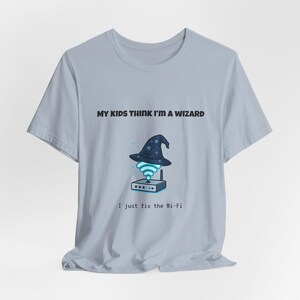 May include: Light blue t-shirt with the text "MY KIDS THINK I'M A WIZARD" above a graphic of a wizard hat over a Wi-Fi router. Below the graphic is the text "I just fix the Wi-Fi".