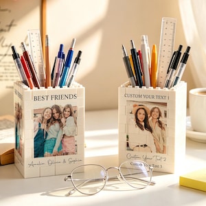 Op de afbeelding: Twee witte rechthoekige pennenbakjes gemaakt van in elkaar grijpende bouwstenen. Elke houder is voorzien van een aangepaste foto aan de voorzijde, met de tekst "BEST FRIENDS" en "Amelia, Olivia & Sophia" op de ene, en "CUSTOM YOUR TEXT 1" op de andere.