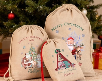 May include: Three beige Christmas gift sacks with drawstring closures. The sacks feature festive illustrations of Santa Claus, reindeer, and Christmas trees. One sack reads "Merry Christmas", another "Special Delivery for Phillips", and the smallest sack has the letter "A" and the name "Anna".