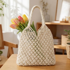 Peut inclure: Un sac fourre-tout en macramé crème avec des anses tressées, rempli d'un bouquet de tulipes colorées. Le sac est en coton tissé et repose sur une table en bois, mettant en valeur un style naturel et bohème.