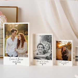 May include: Four white rectangular building block frames of varying heights, each displaying a unique photograph. The base of each frame features printed names, a date, and a small heart icon. The frames are arranged in a descending height order.
