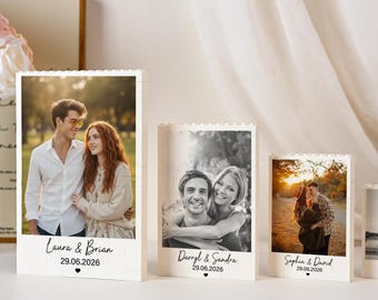 May include: Four white rectangular building block frames of varying heights, each displaying a unique photograph. The base of each frame features printed names, a date, and a small heart icon. The frames are arranged in a descending height order.